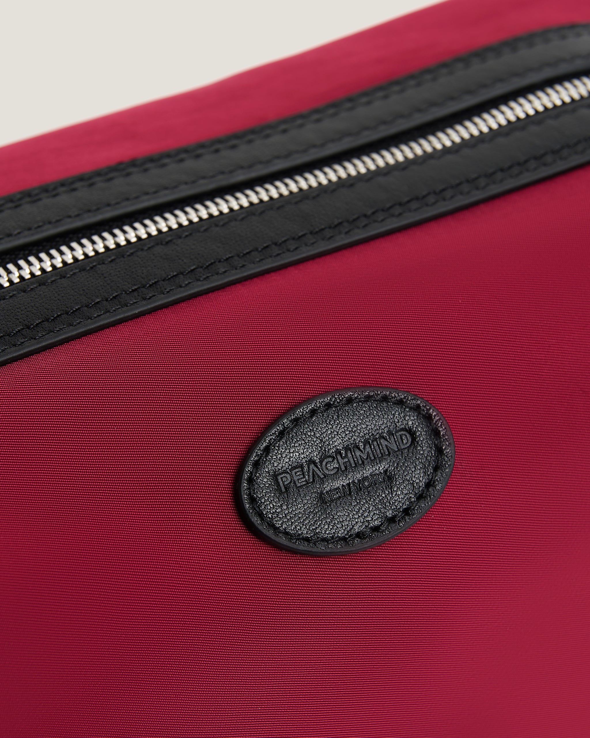 red nylon toiletry bag with a silver zipper and a visible PEACHMIND logo on a light gray background
