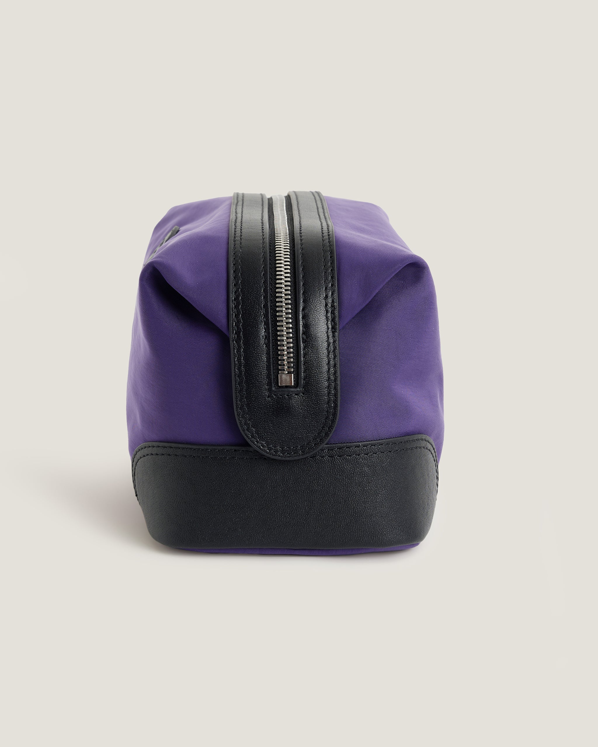 Purple toiletry bag with black zipper and base on a beige background