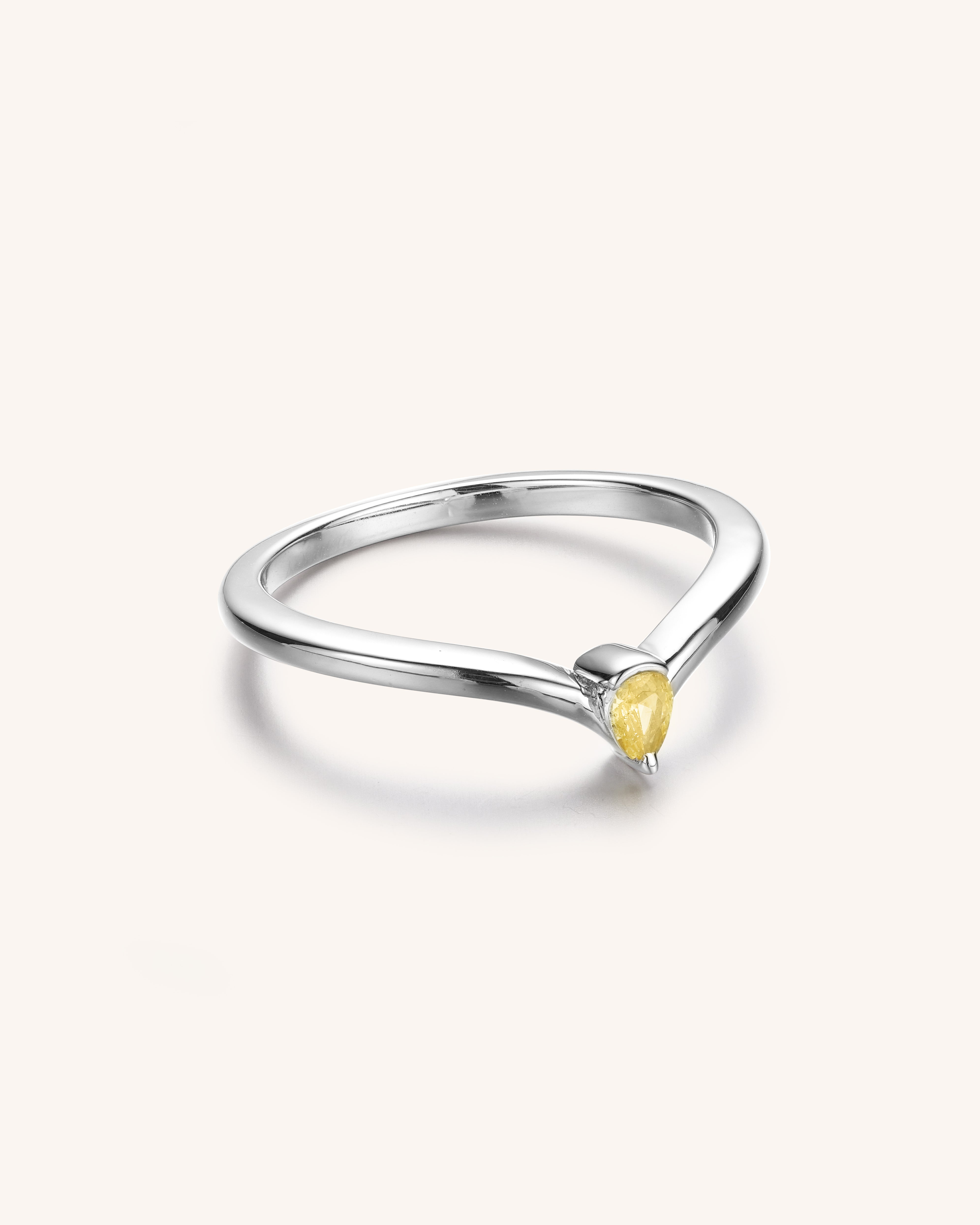A silver ring with a pear cut yellow stone in the center.