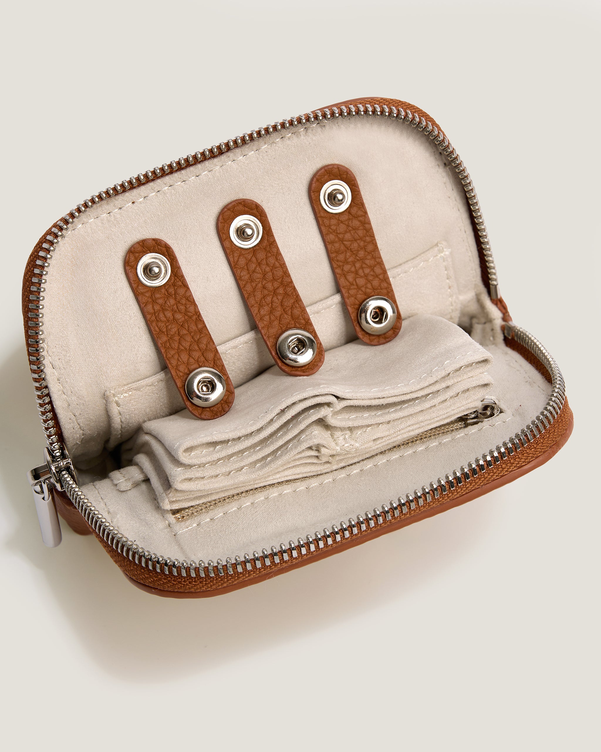 Small beige pouch with brown leather straps and metal clasps on a light gray background