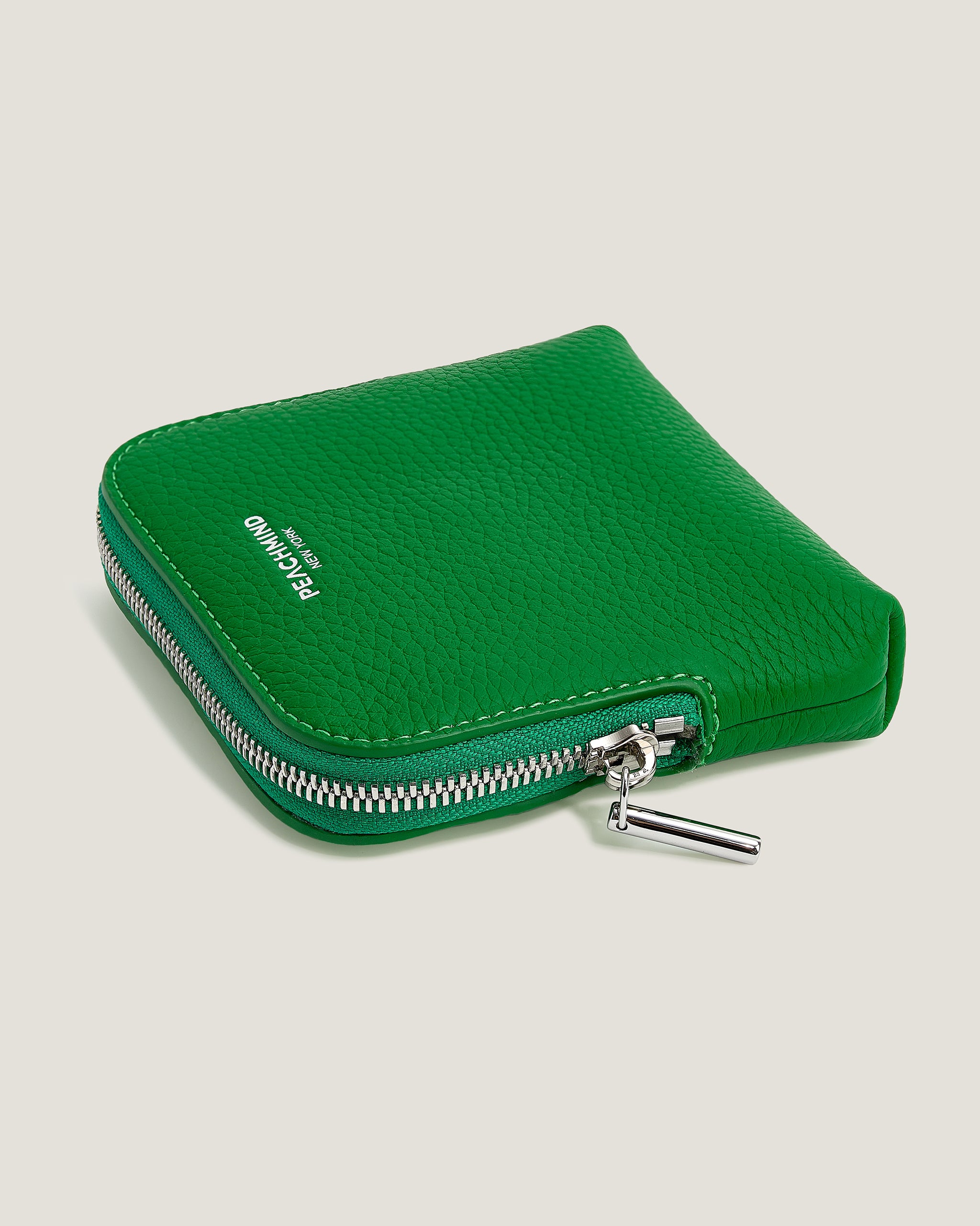 Green zippered pouch with a brand logo on a beige background
