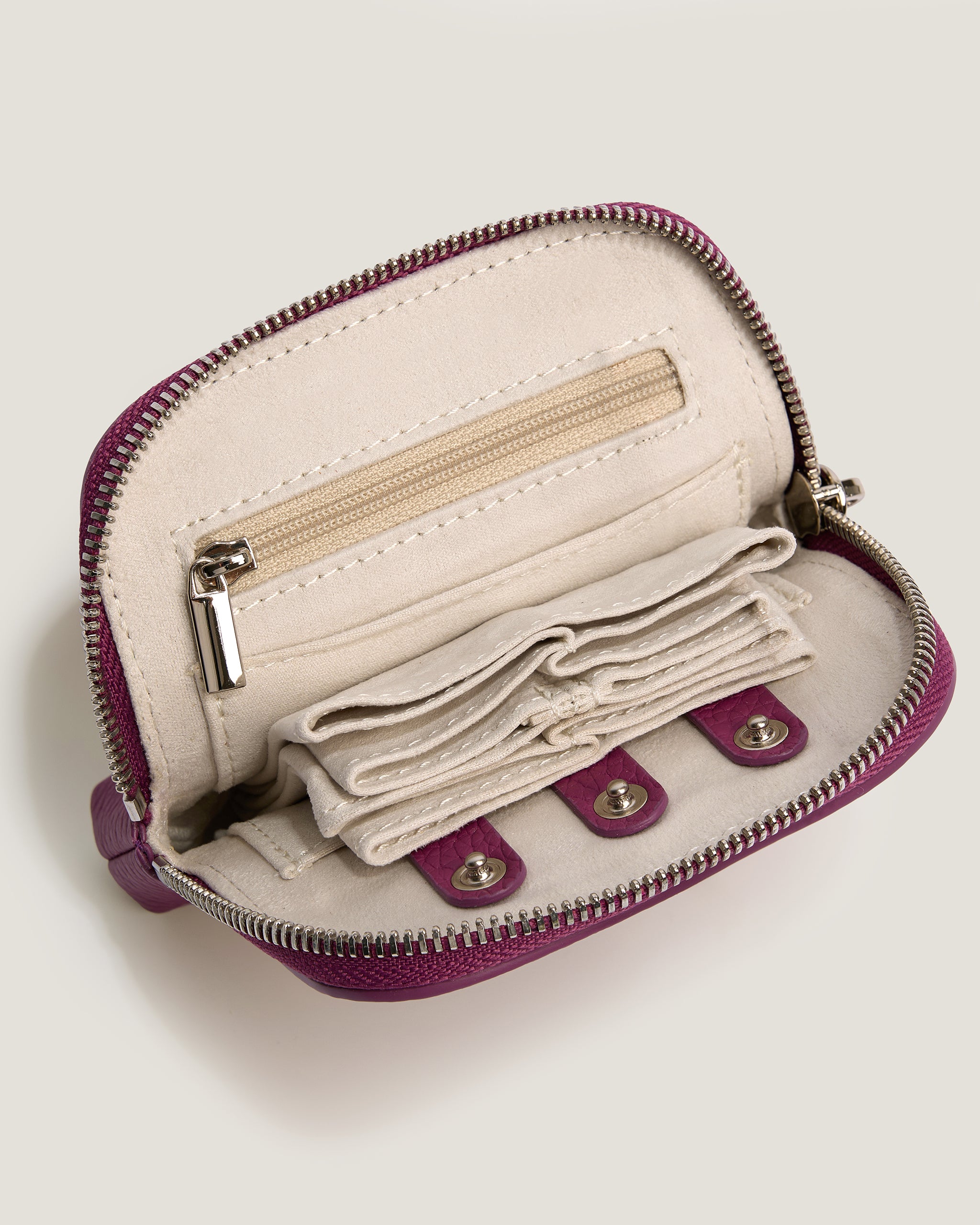Small beige purse with purple zipper and interior lining on a light gray background