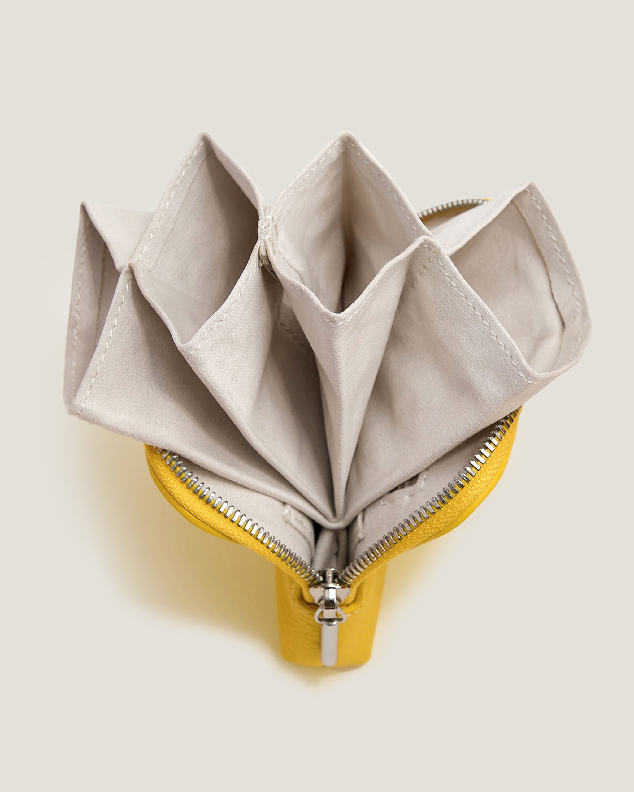 Open beige pouch with a yellow zipper on a light beige background
