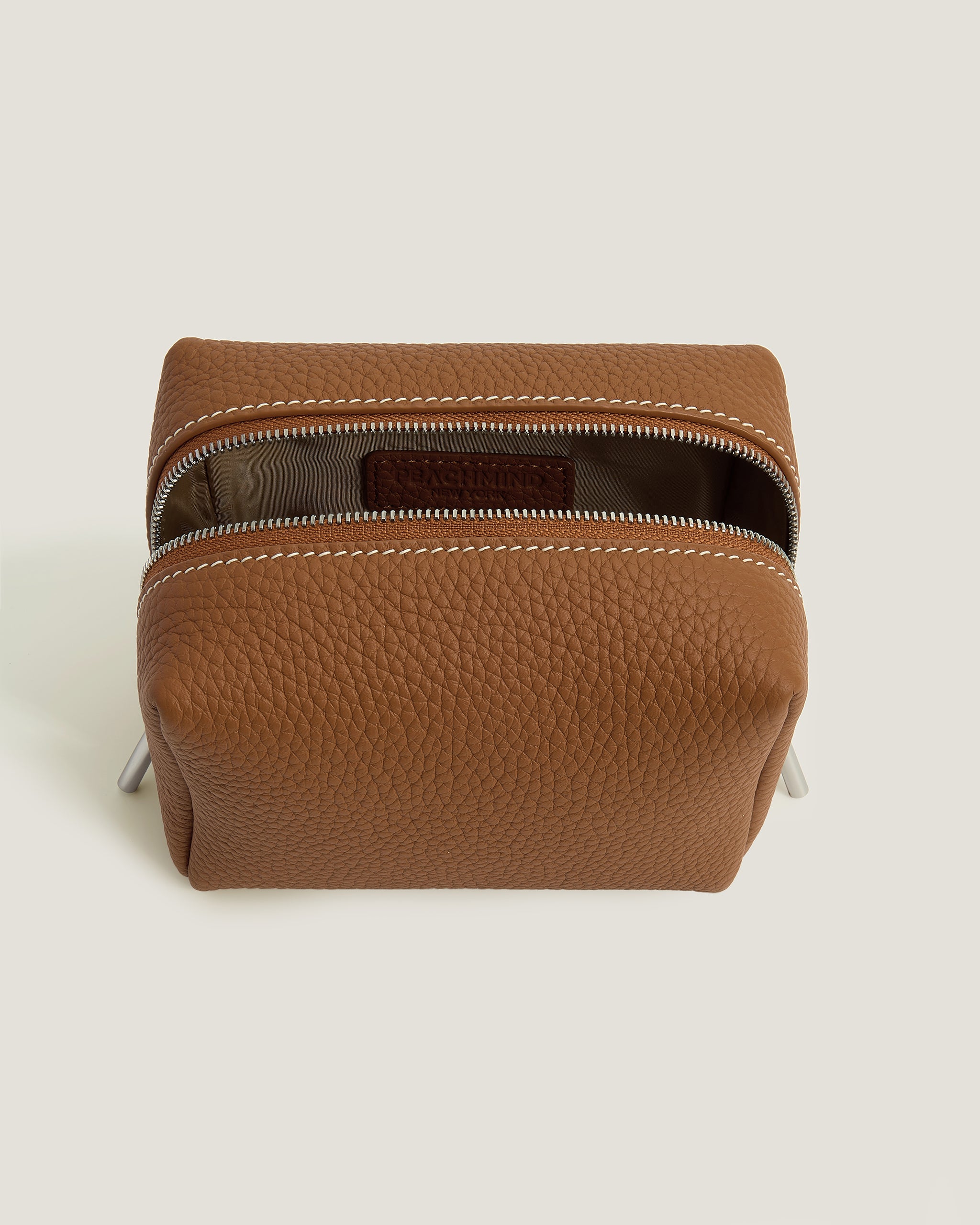 Brown leather pouch with zipper on a light beige background