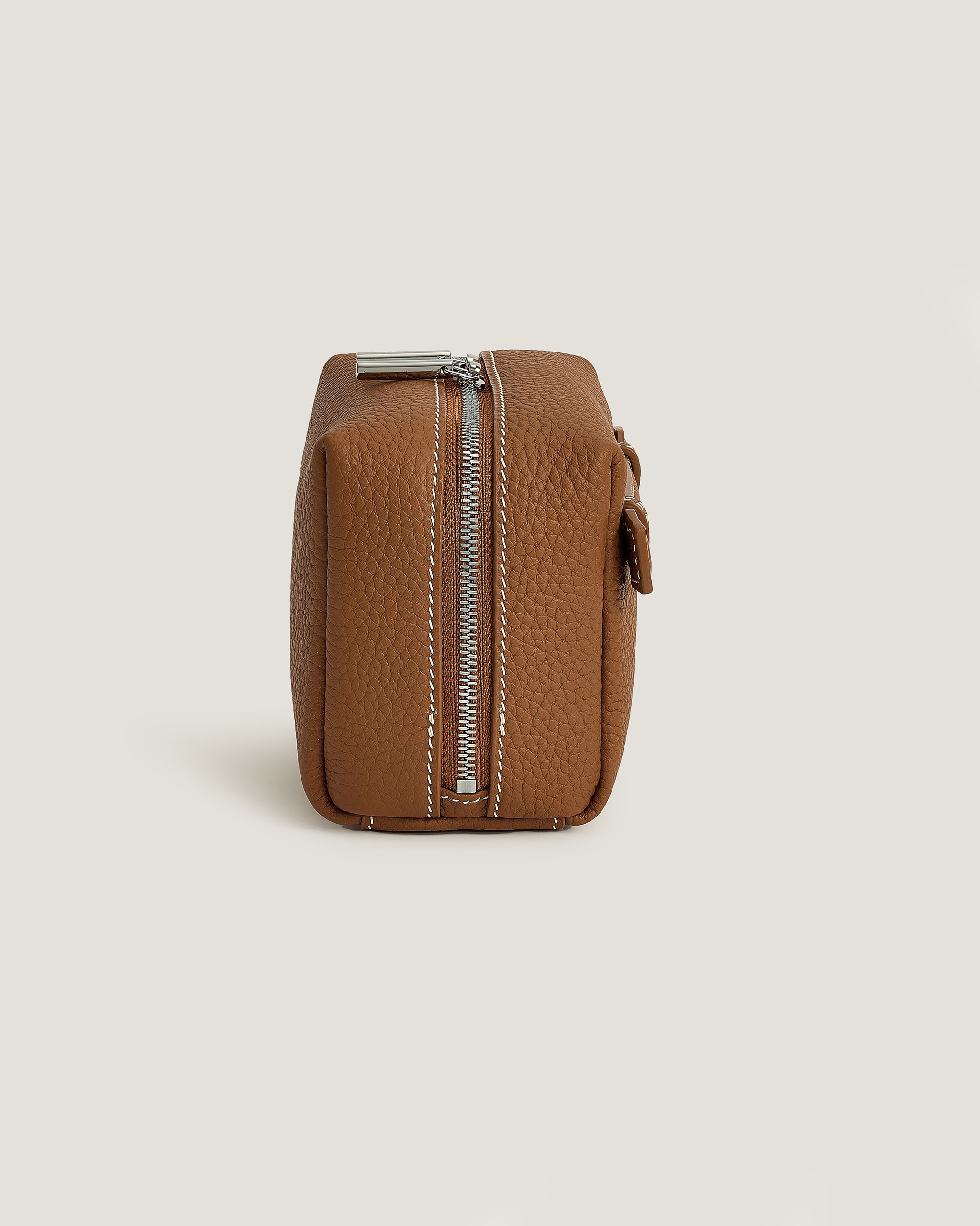 Brown leather makeup pouch with a zipper on a beige background
