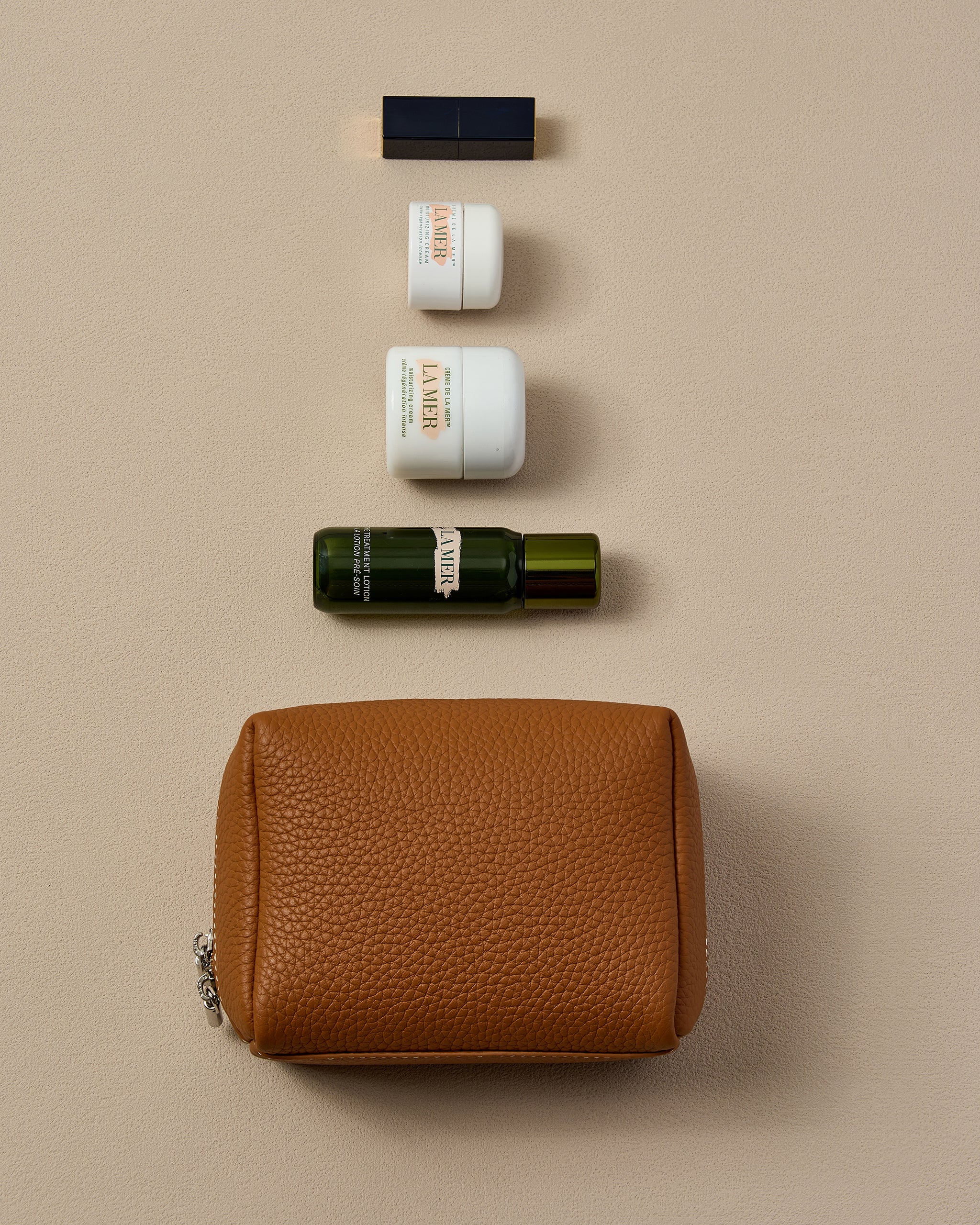 Cosmetic products including a brown leather pouch, bottles, and containers on a beige background