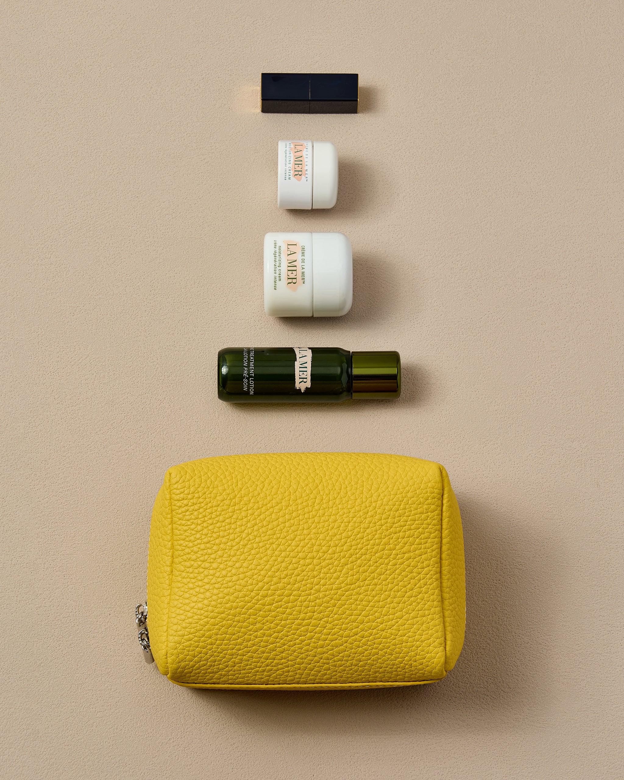 Set of skincare products on a beige background with a yellow makeup mini pouch.