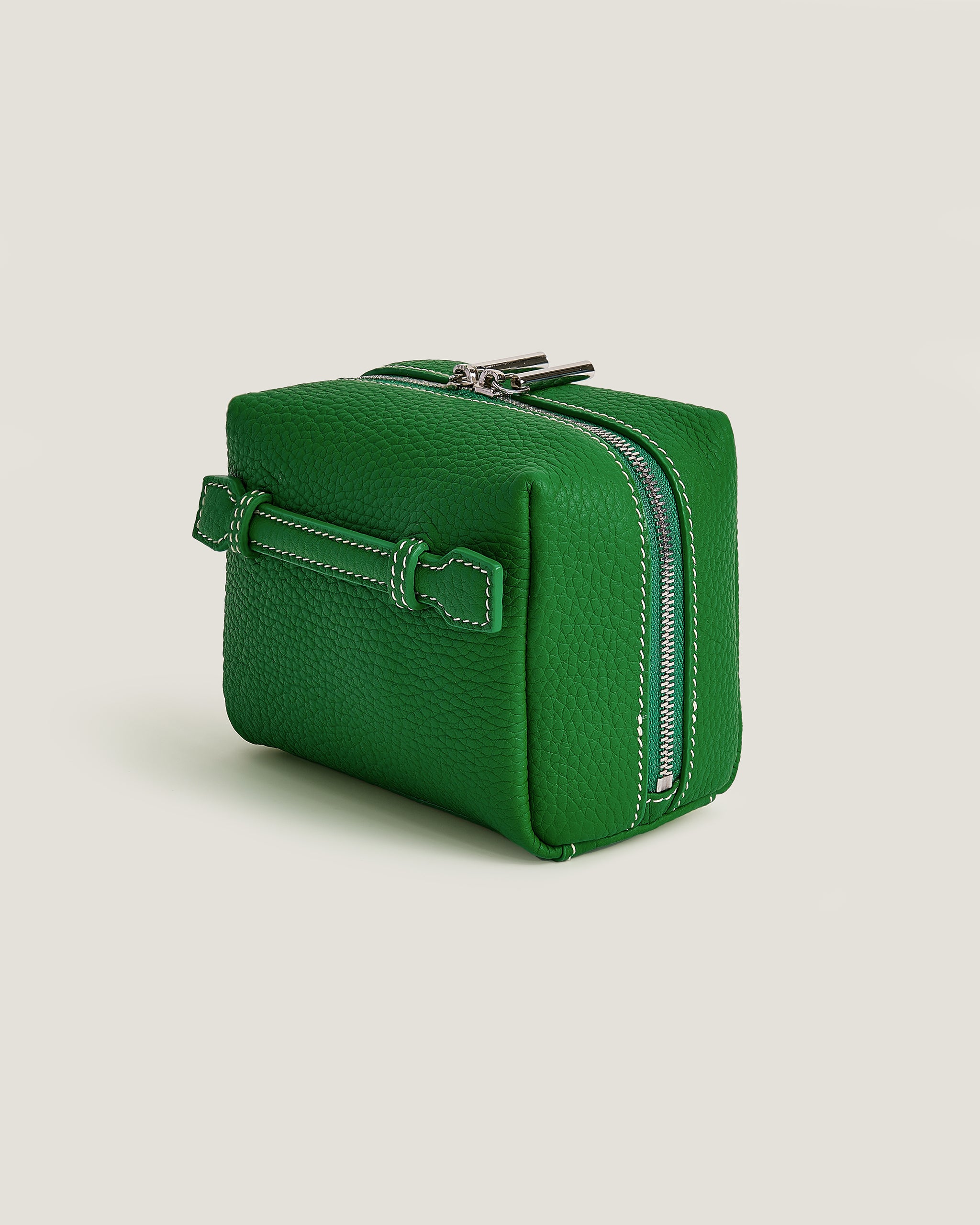 Green leather bag with a silver zipper on a beige background