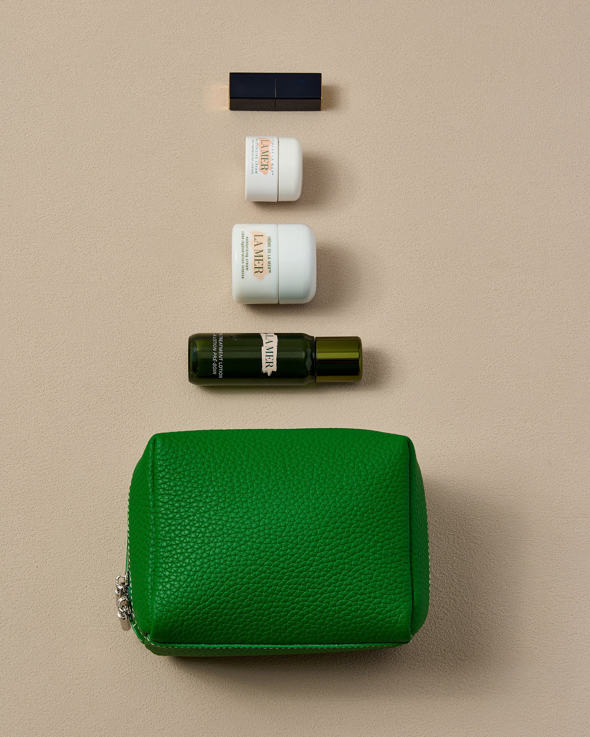 Green leather pouch with skincare products on a beige background