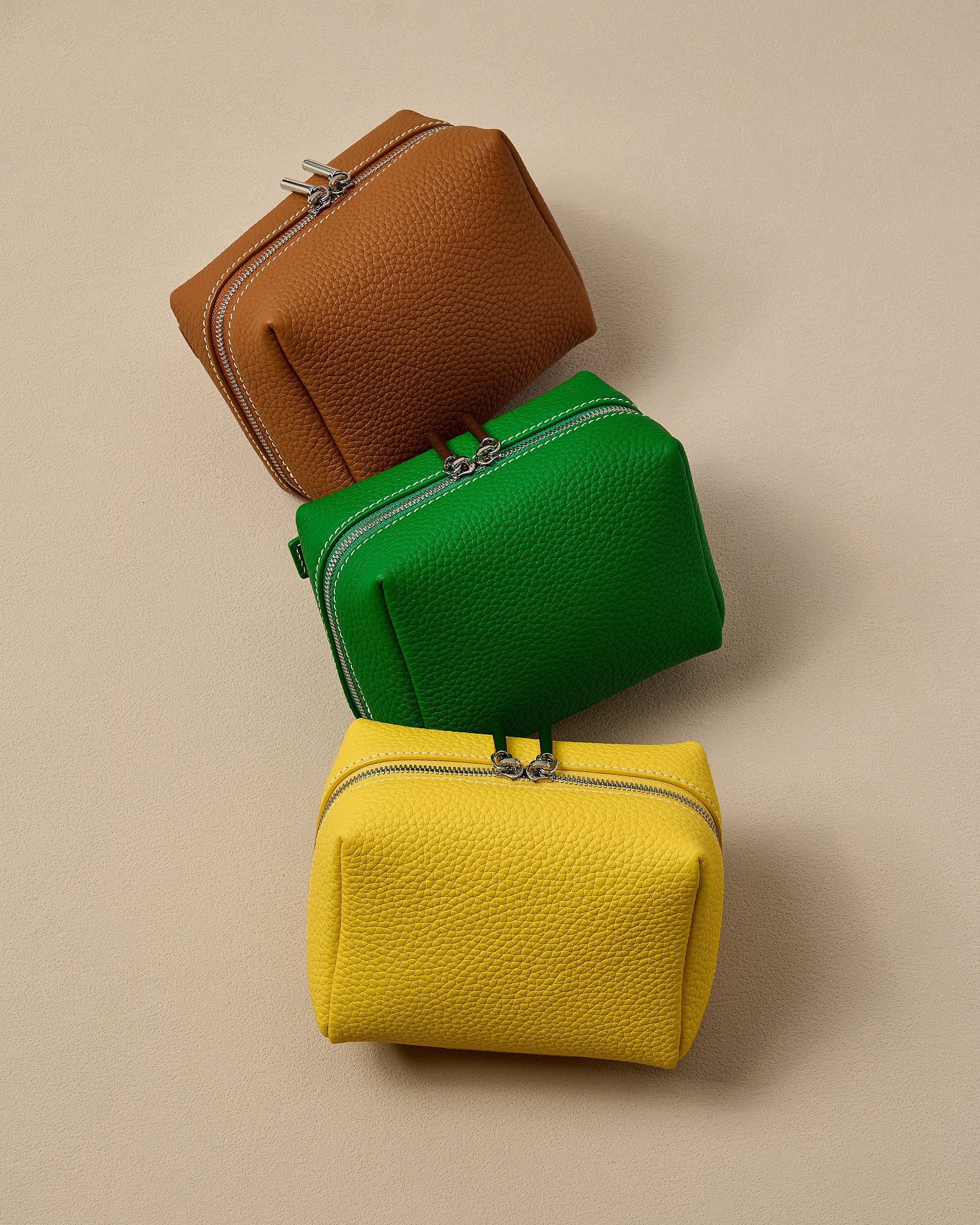 Three leather pouchs in brown, green, and yellow stacked on a beige background