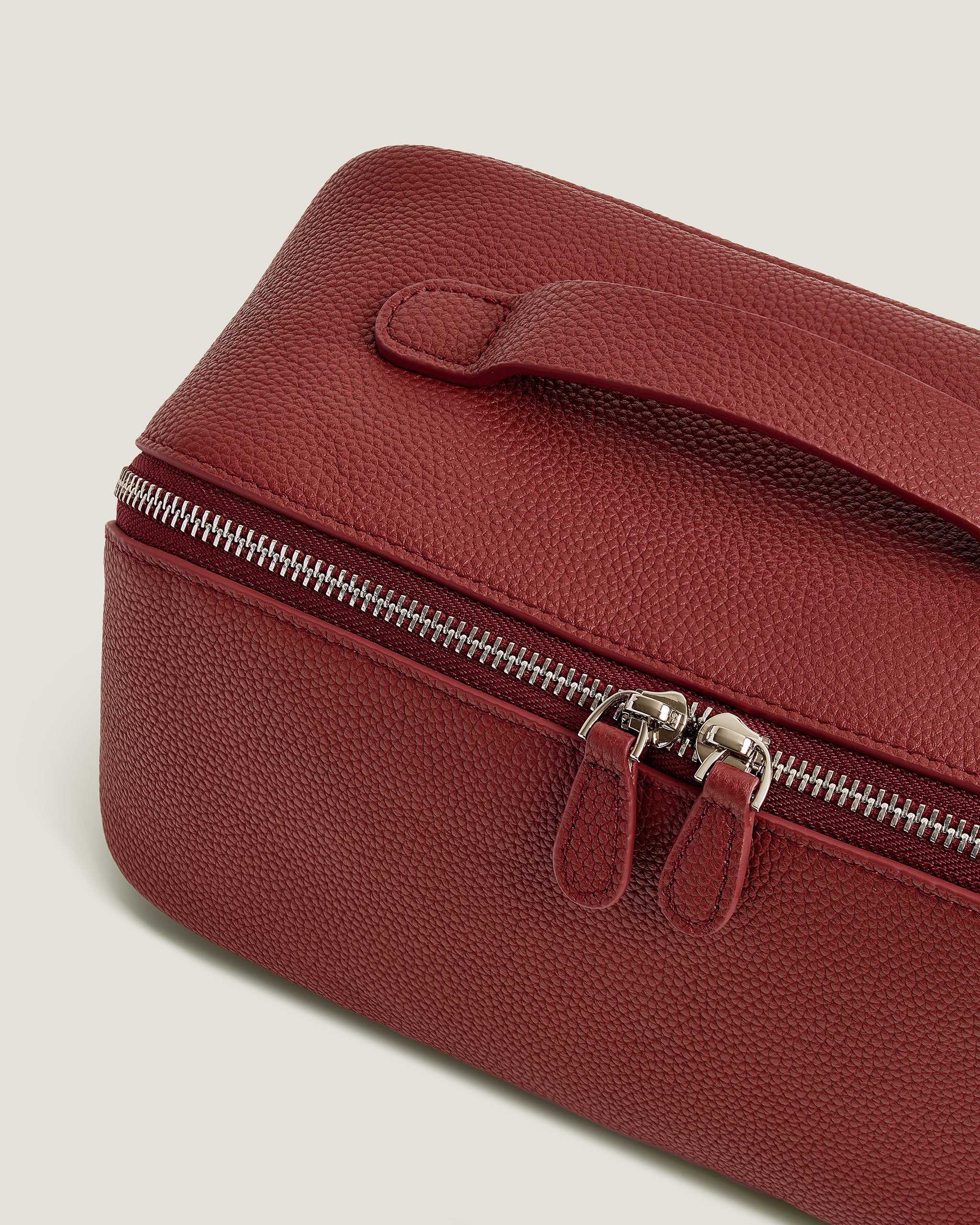Red leather makeup bag with a silver zipper on a light gray background