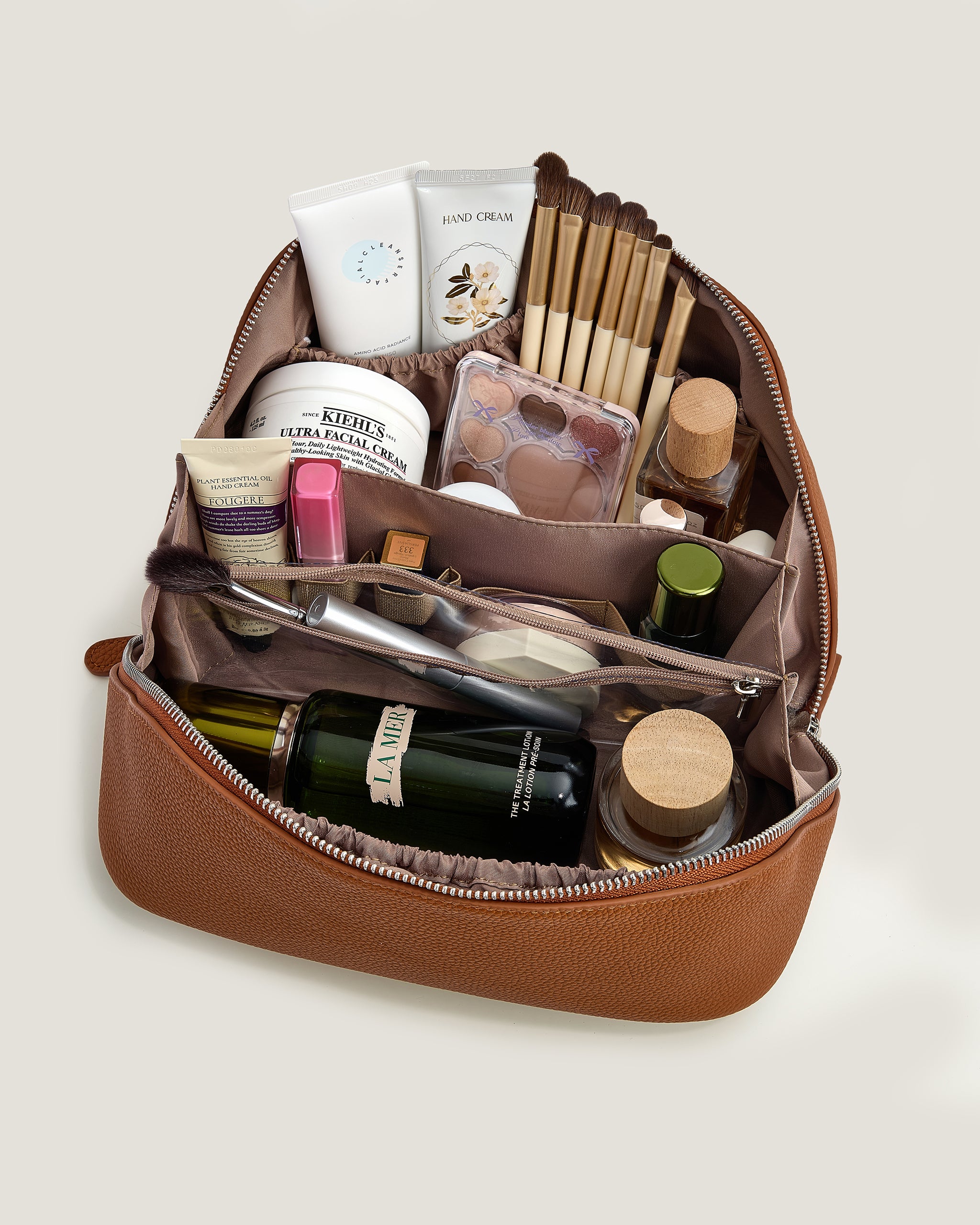 Open brown leather cosmetic bag with various items on a light beige background
