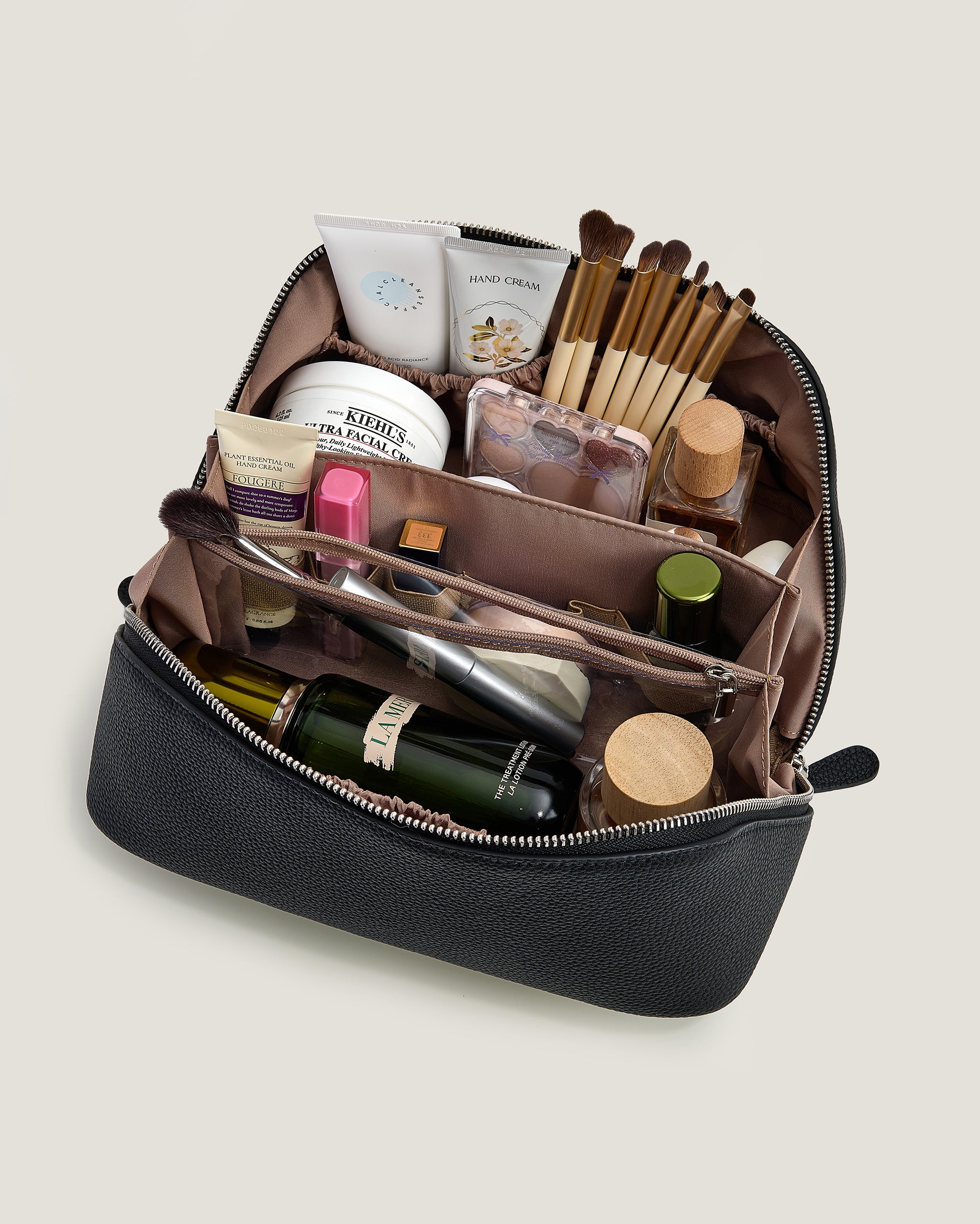 Open black cosmetic bag with various items on a light beige background