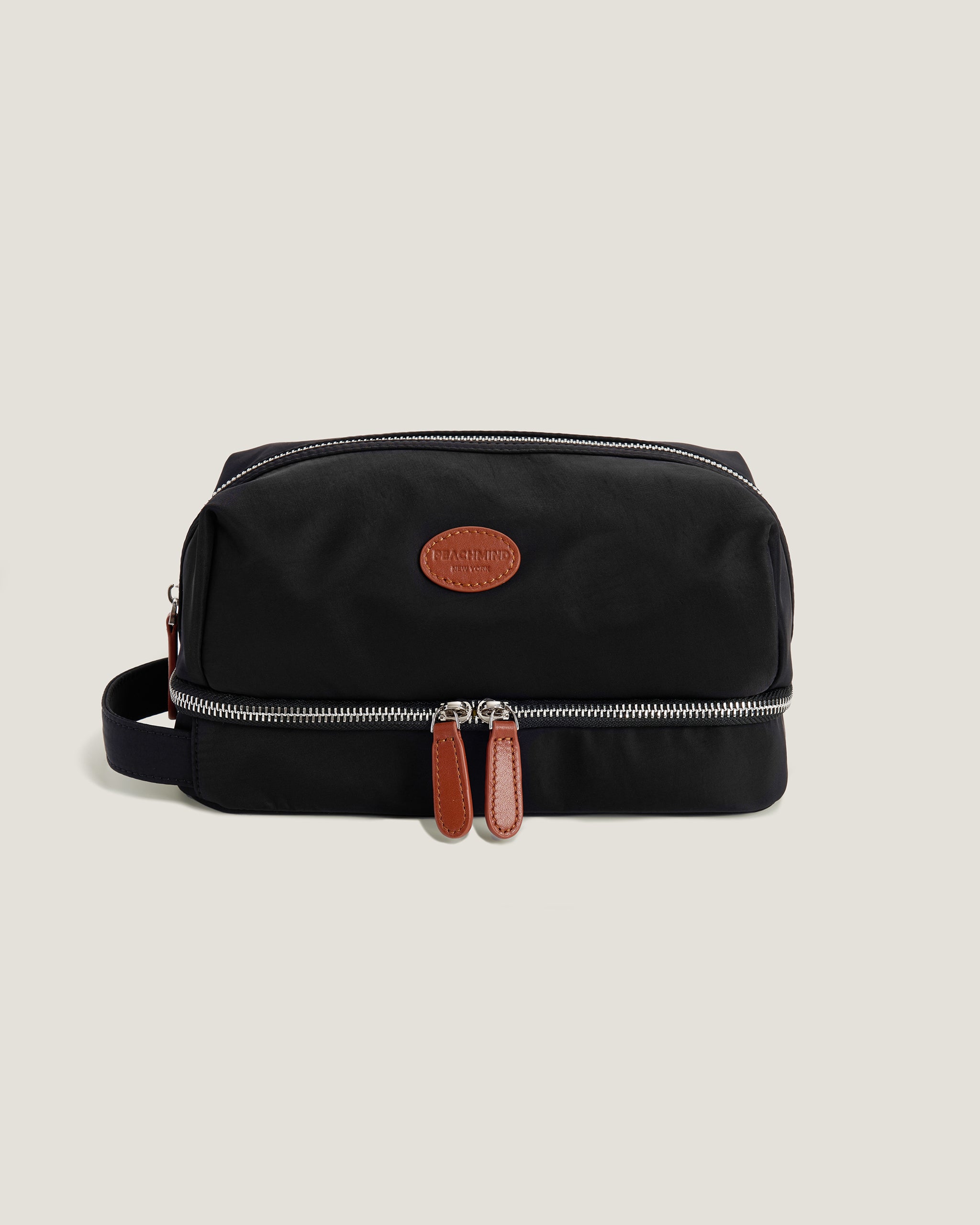 Black toiletry bag with brown leather straps on a beige background