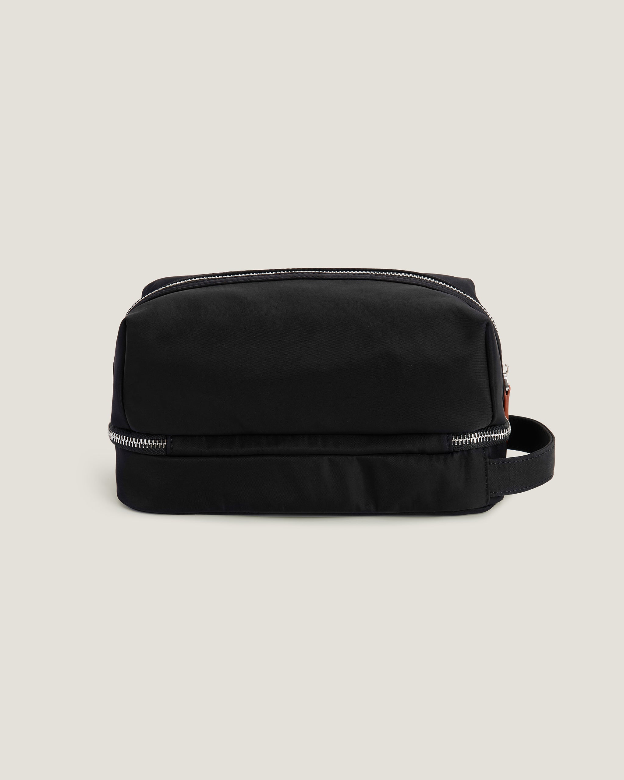 Black toiletry bag with brown leather straps on a beige background