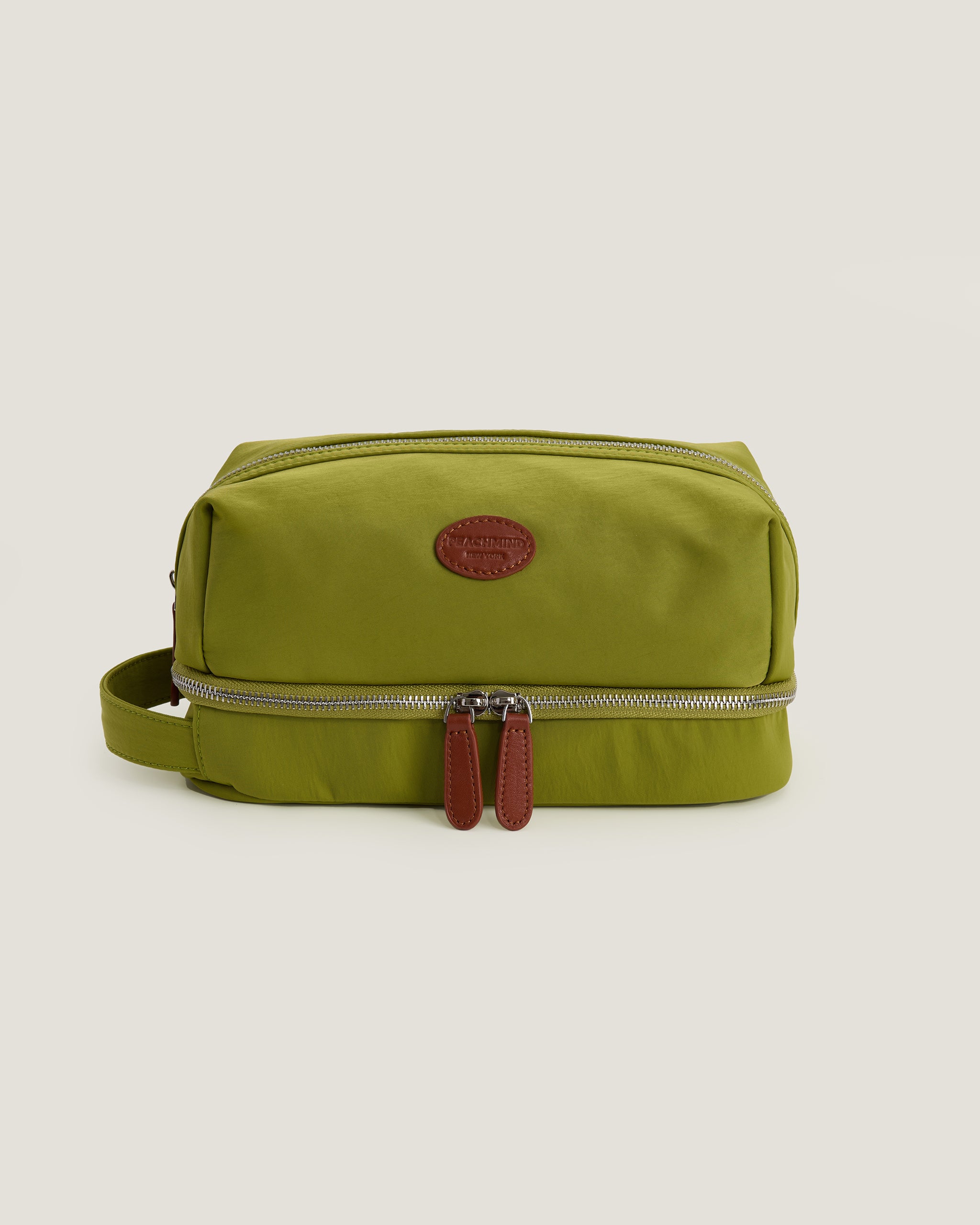 Green toiletry bag with a brown zipper on a beige background