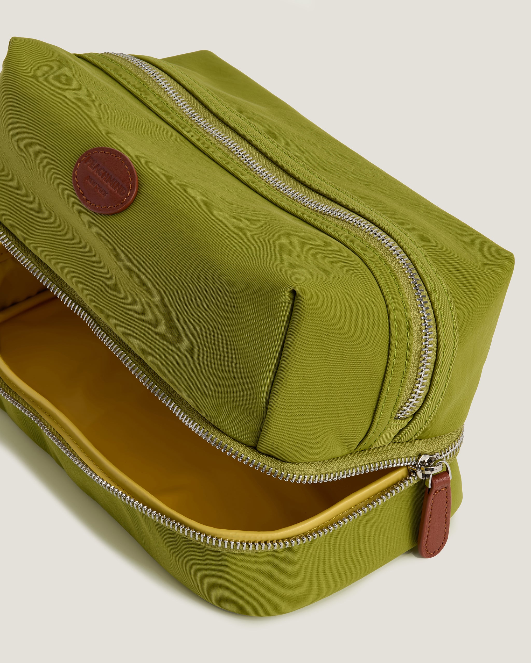 Green toiletry bag with a brown interior and zipper on a light gray background