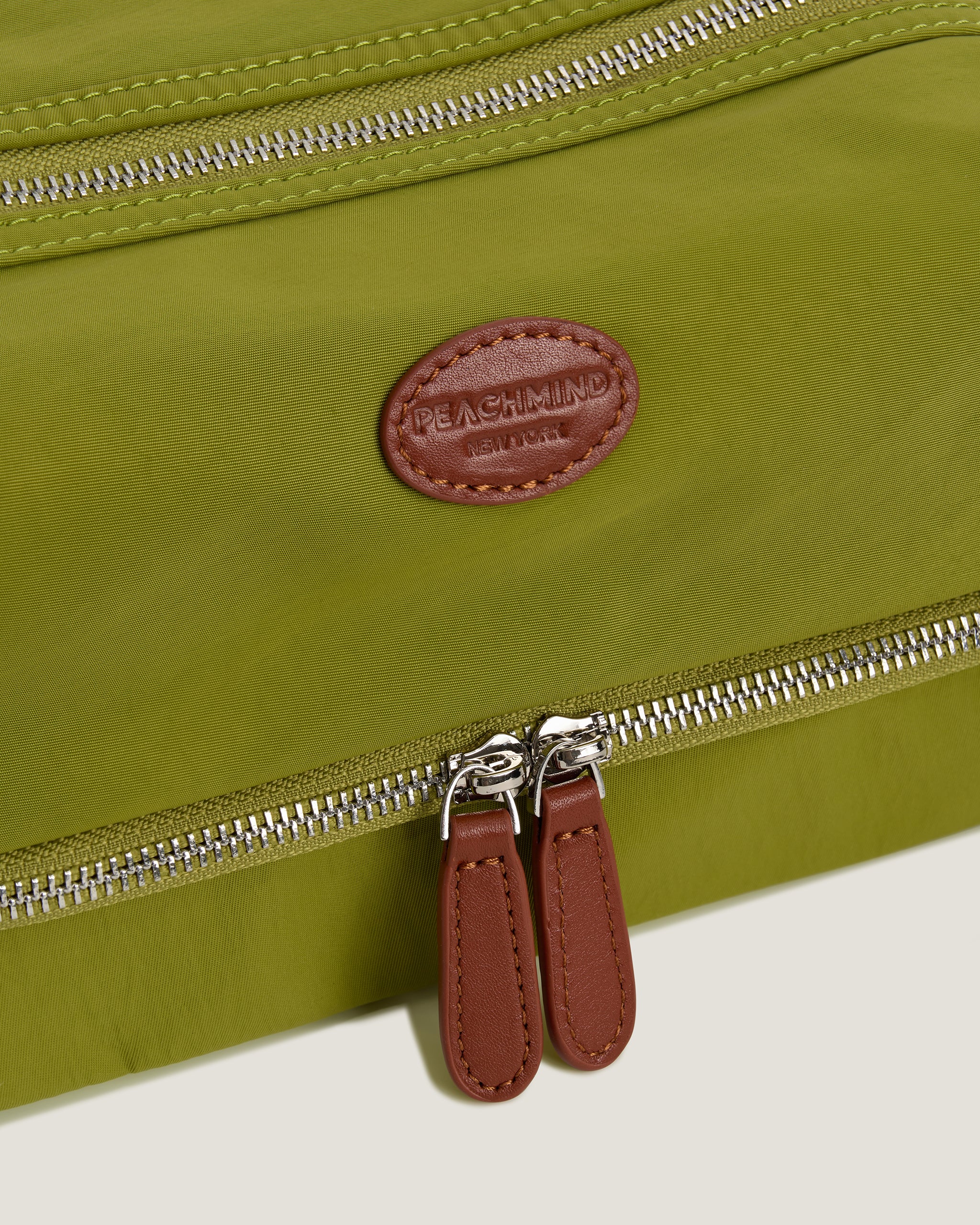 Green bag with a brown leather tag and zipper details on a white background