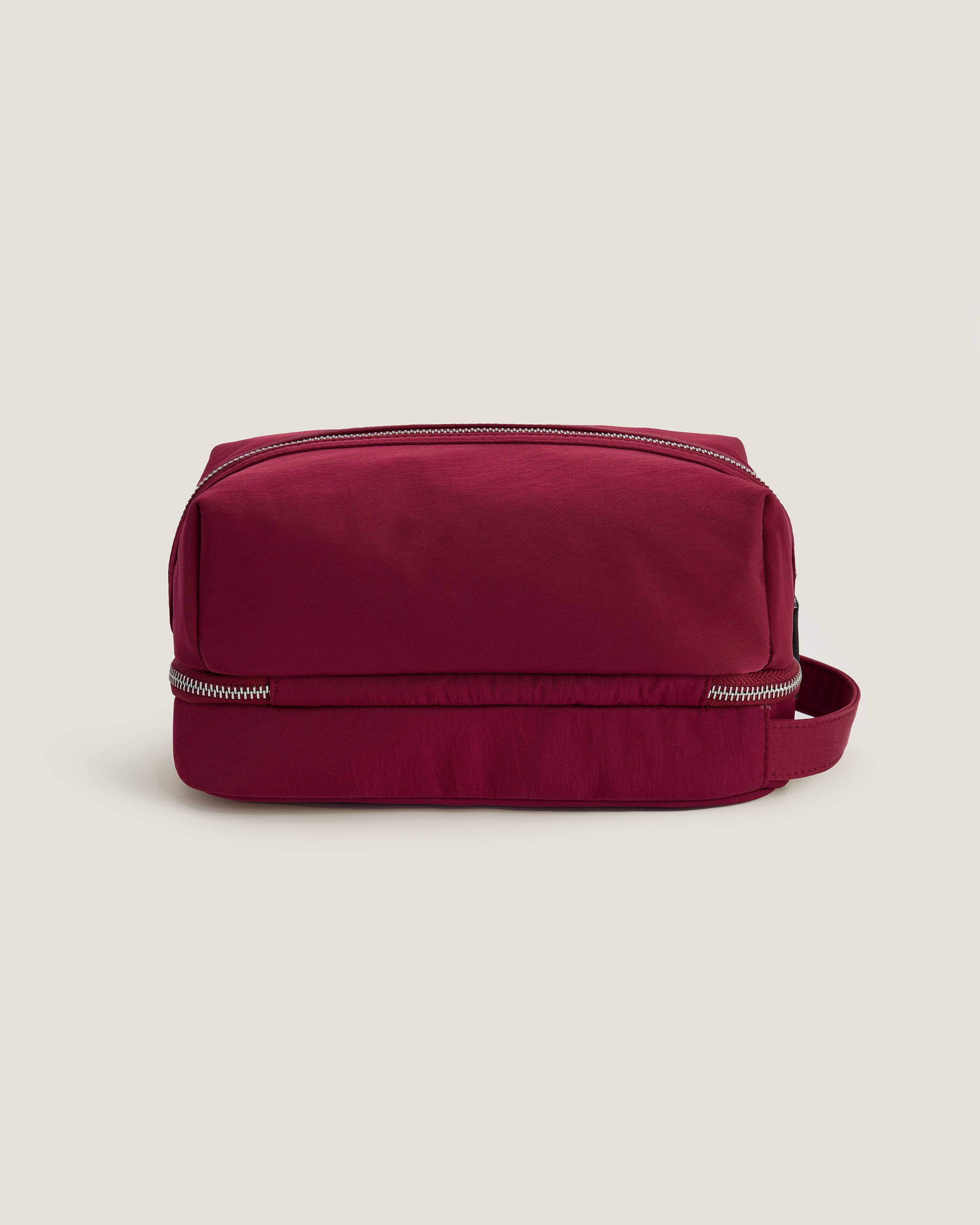Red toiletry bag with a strap on a beige background