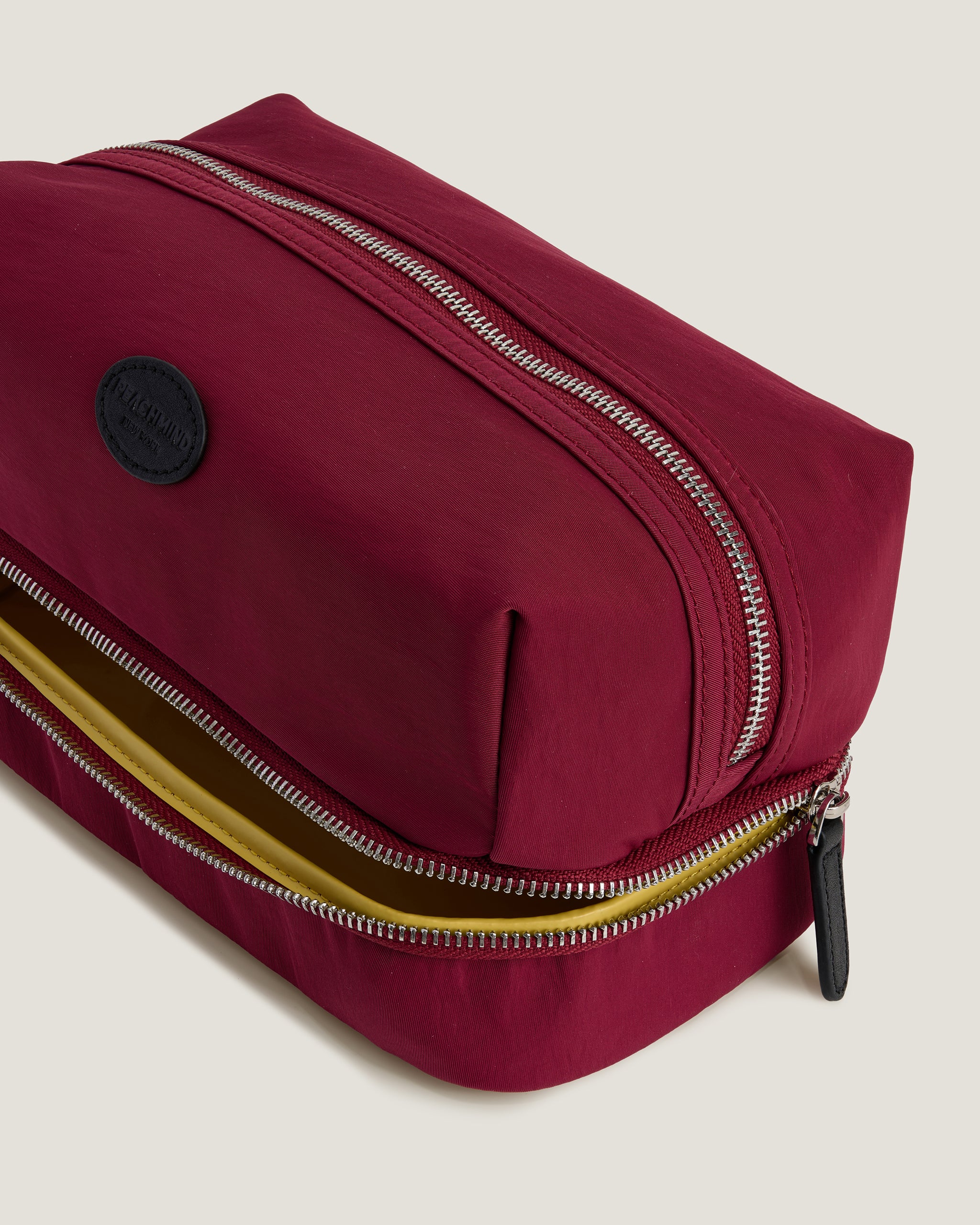 Maroon toiletry bag with gold zipper on a beige background