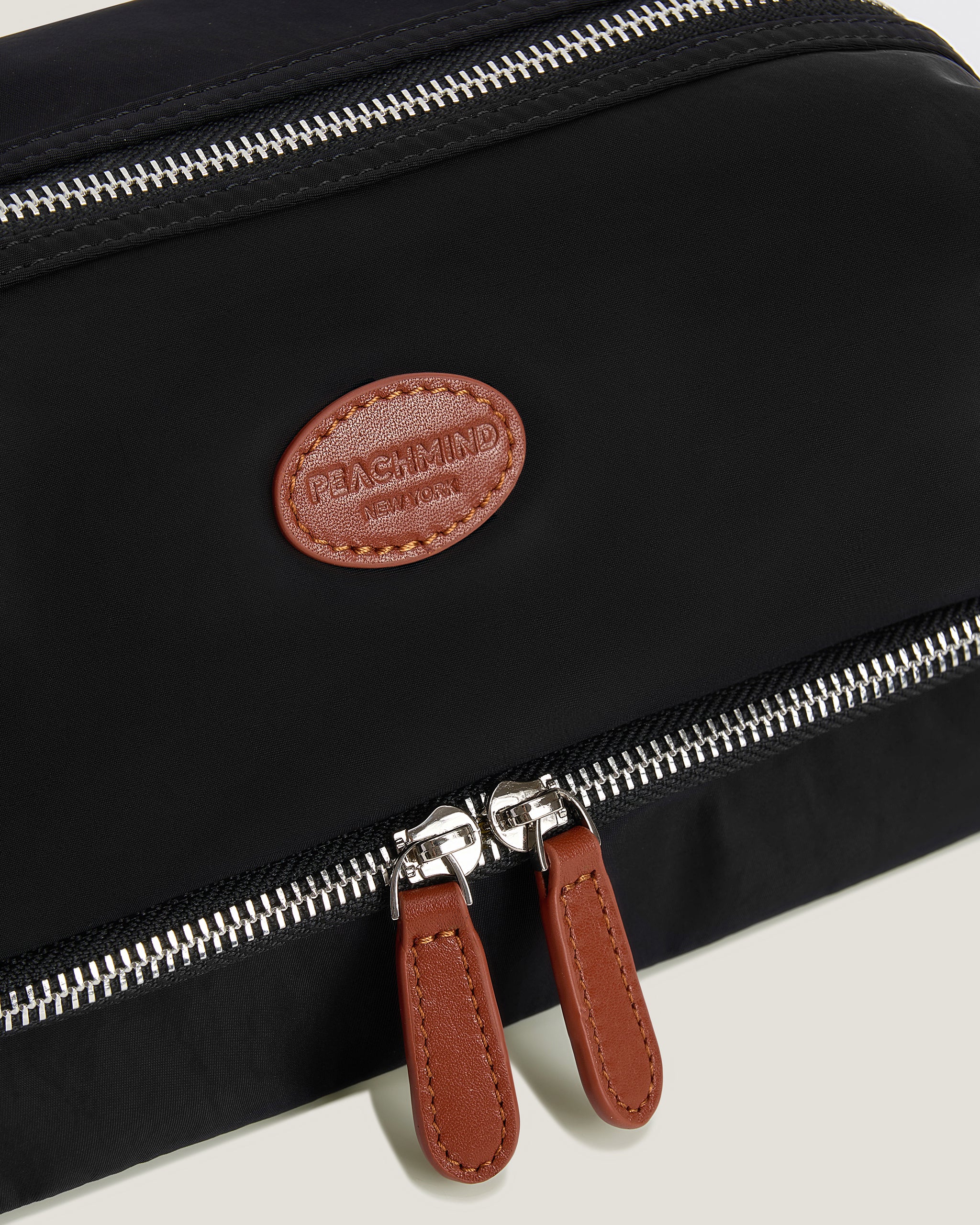 Black bag with a brown Peachmind leather patch and zipper details on a light gray background