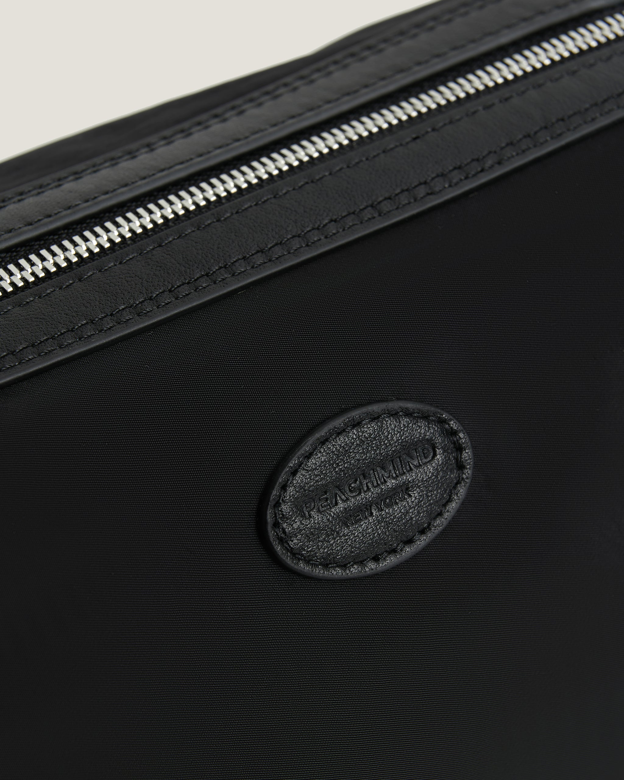 Black leather bag with a silver zipper and a visible PEACHMIND logo 