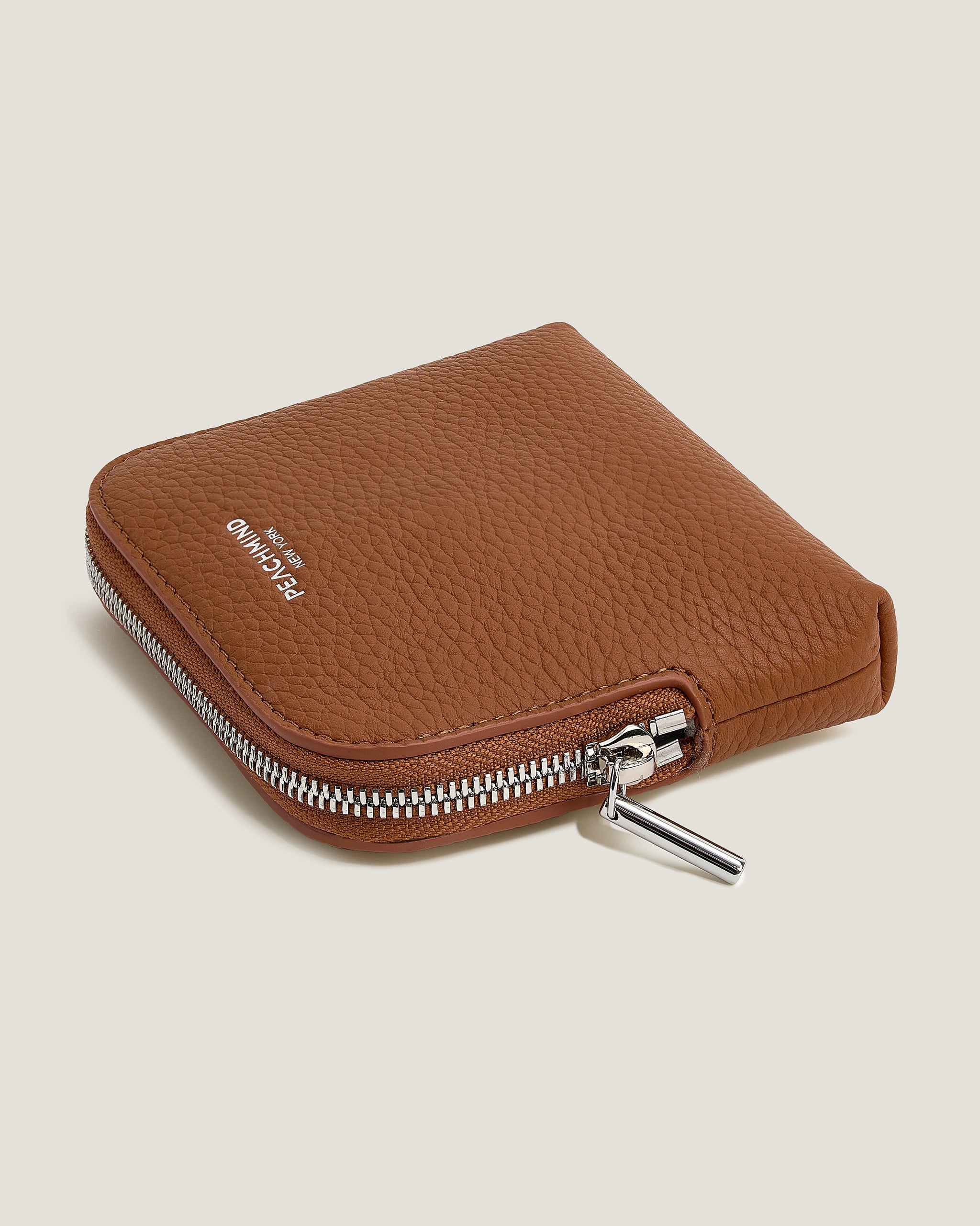 Brown leather zippered wallet on a beige background
