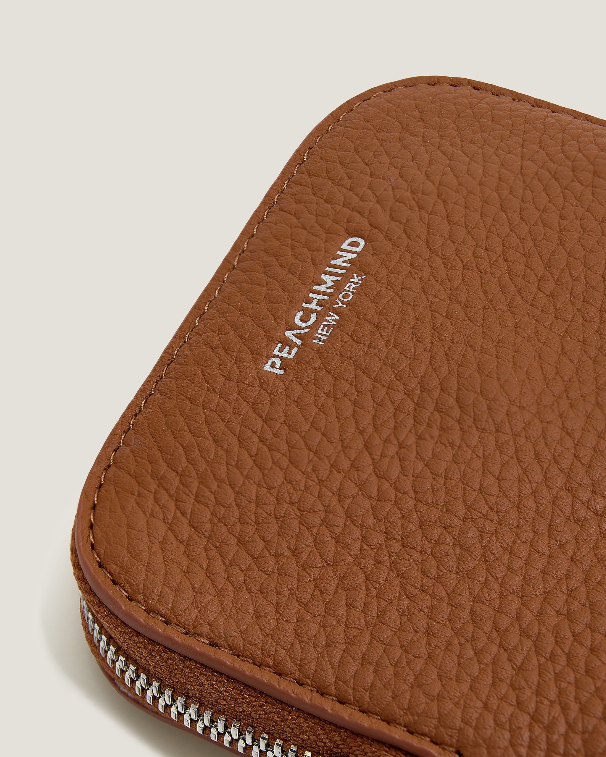 Brown leather pouch with 'Peachmind New York' branding on a beige background