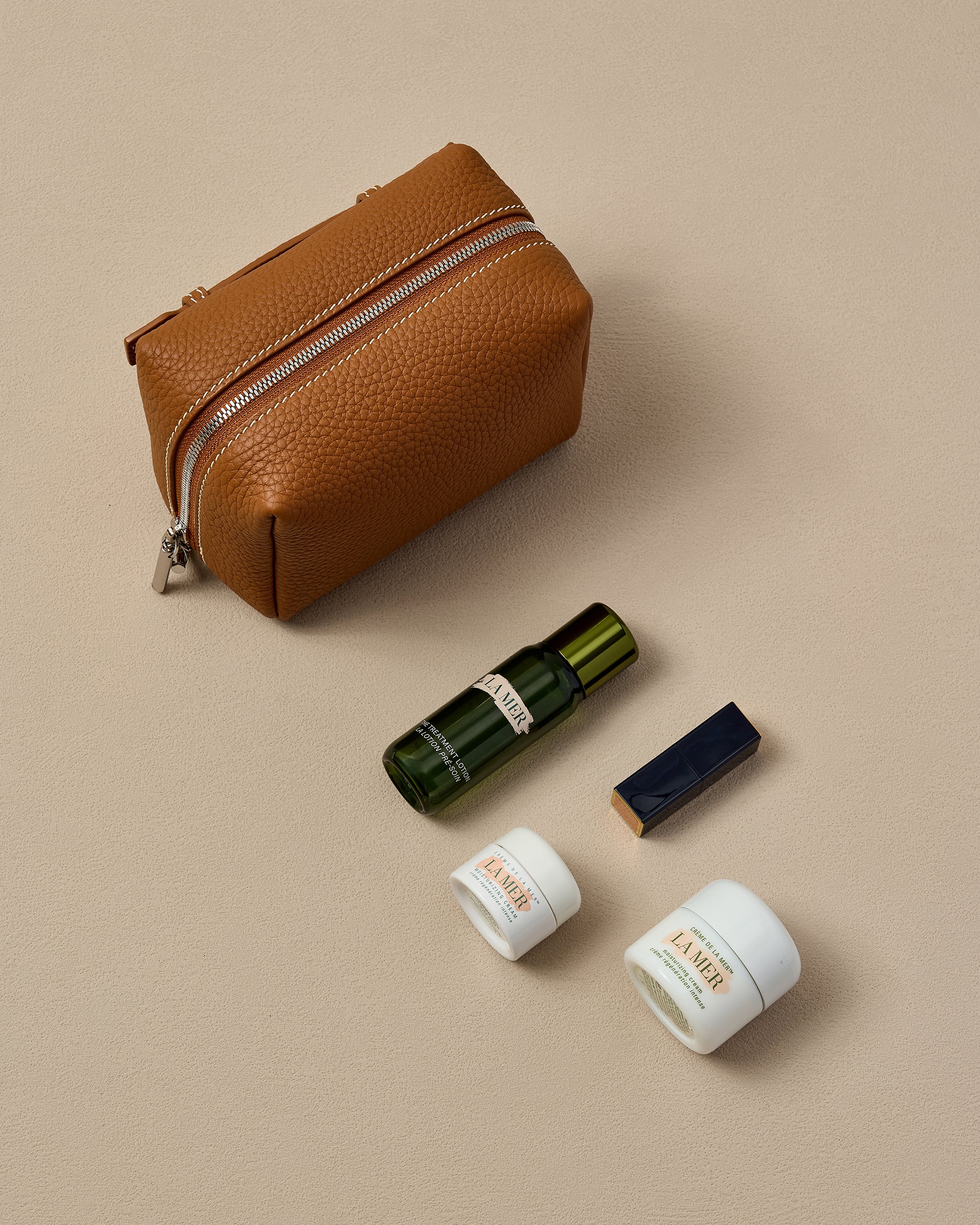 Brown leather pouch with cosmetic bottles on a beige background