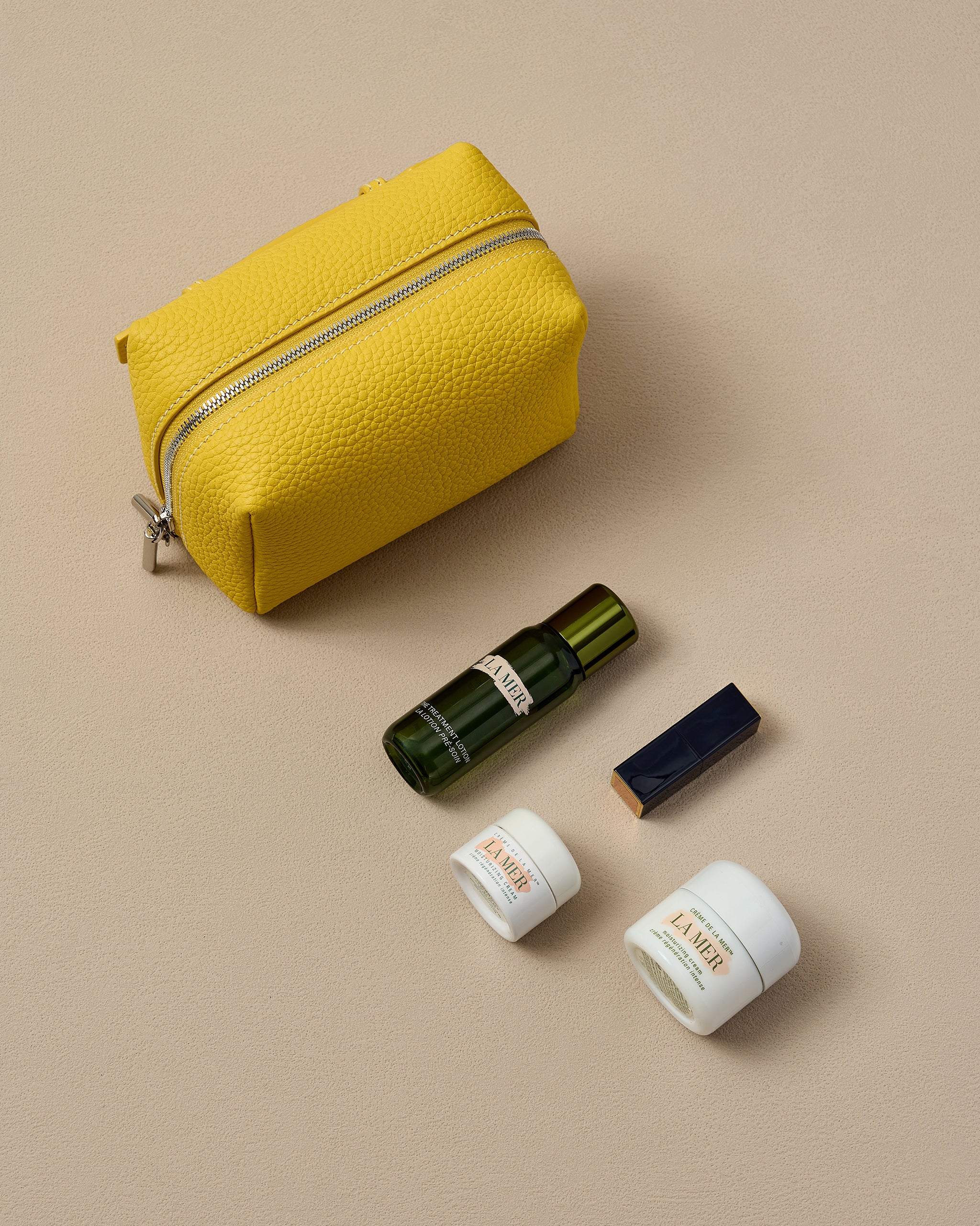 Yellow mini makeup pouch with skincare products on a beige background