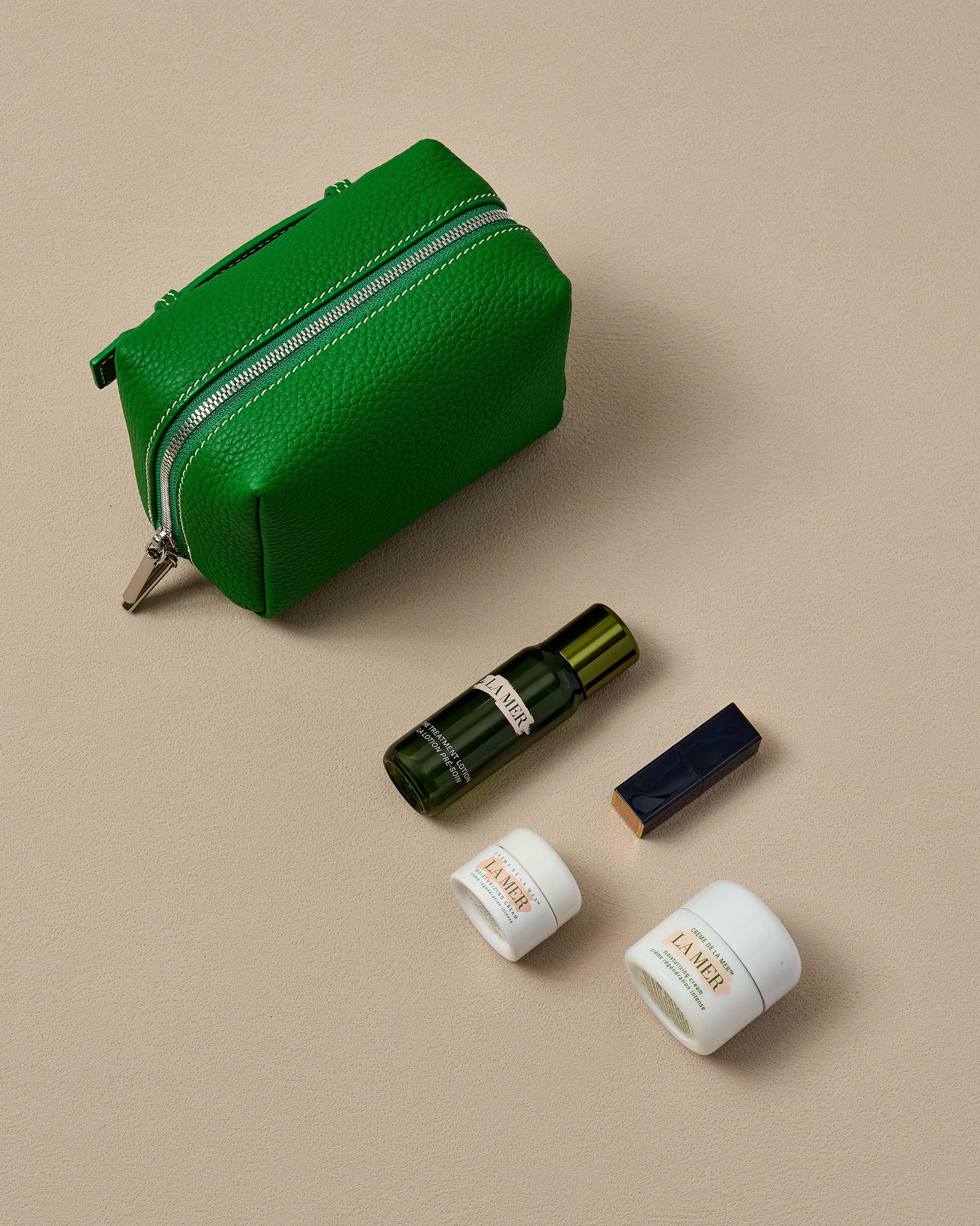 Green cosmetic pouch with skincare products on a beige background