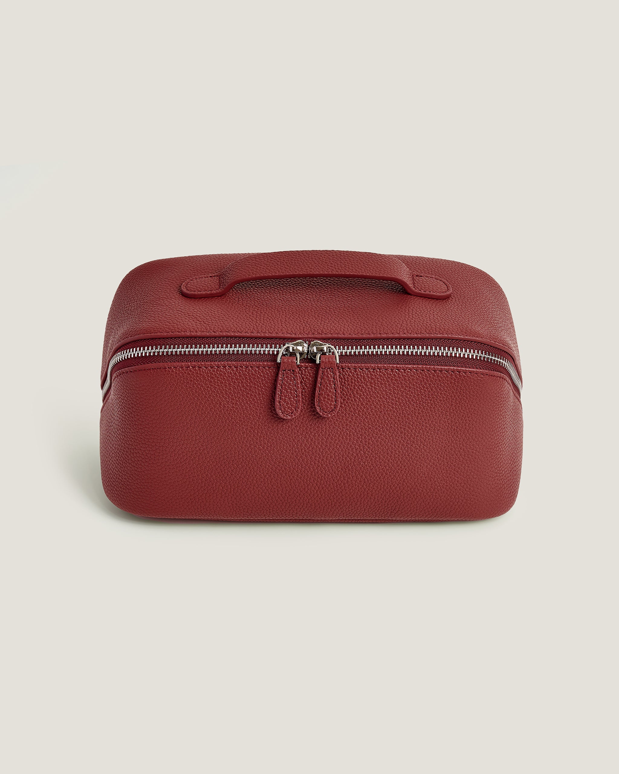 Red leather travel case with a zipper on a beige background