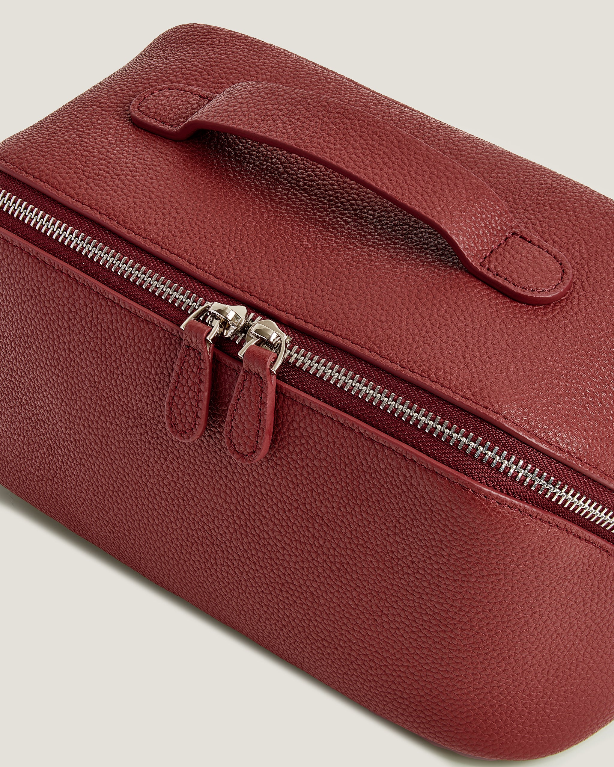 Red leather makup bag with a silver zipper on a light gray background