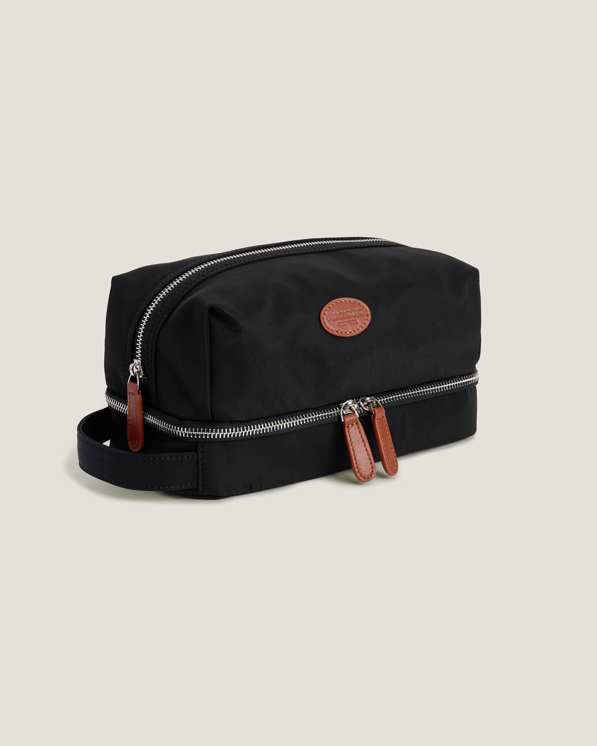 Black toiletry bag with brown leather straps on a beige background