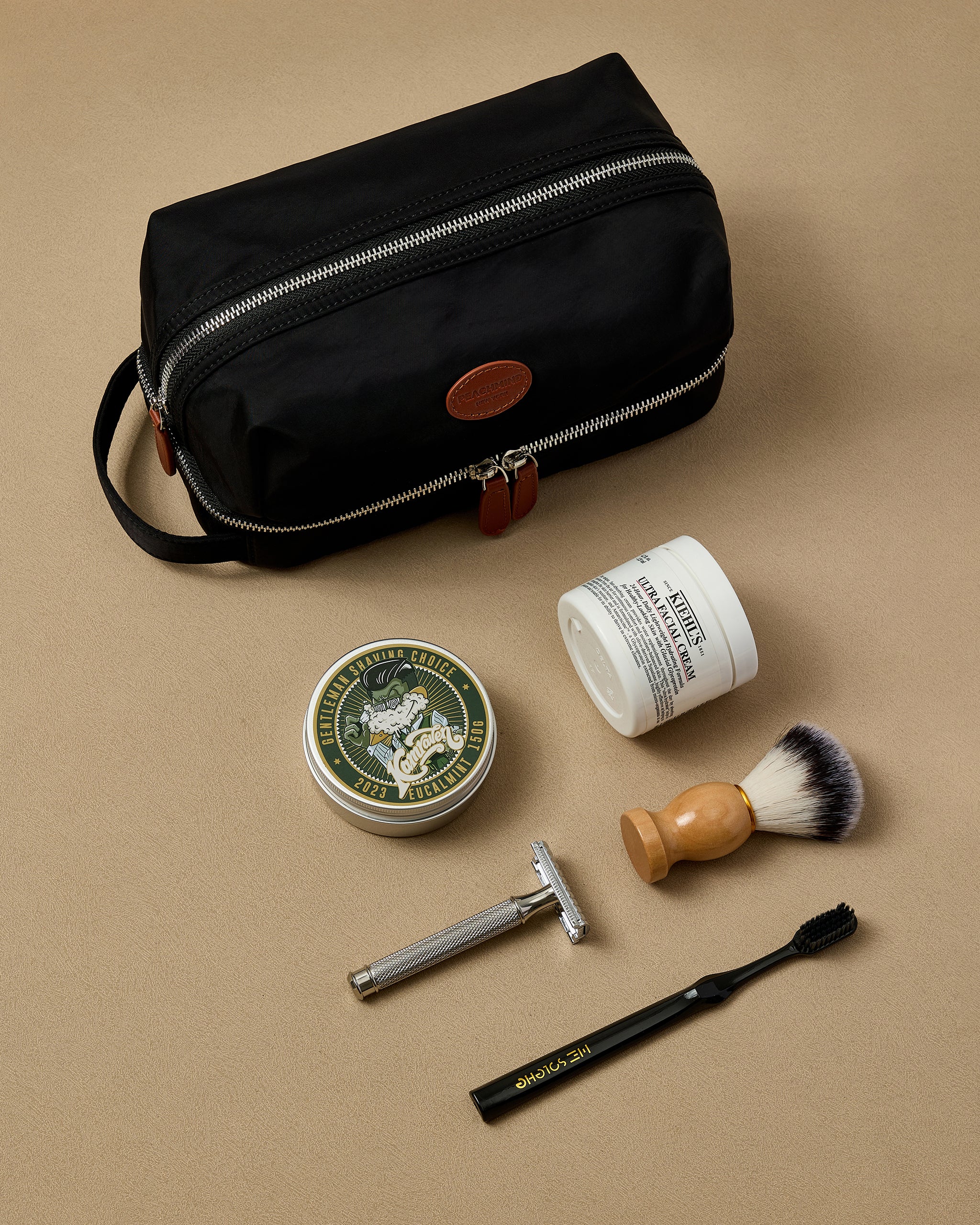 Shaving kit with black toiletry bag, shaving cream, brush, and razor on a beige background