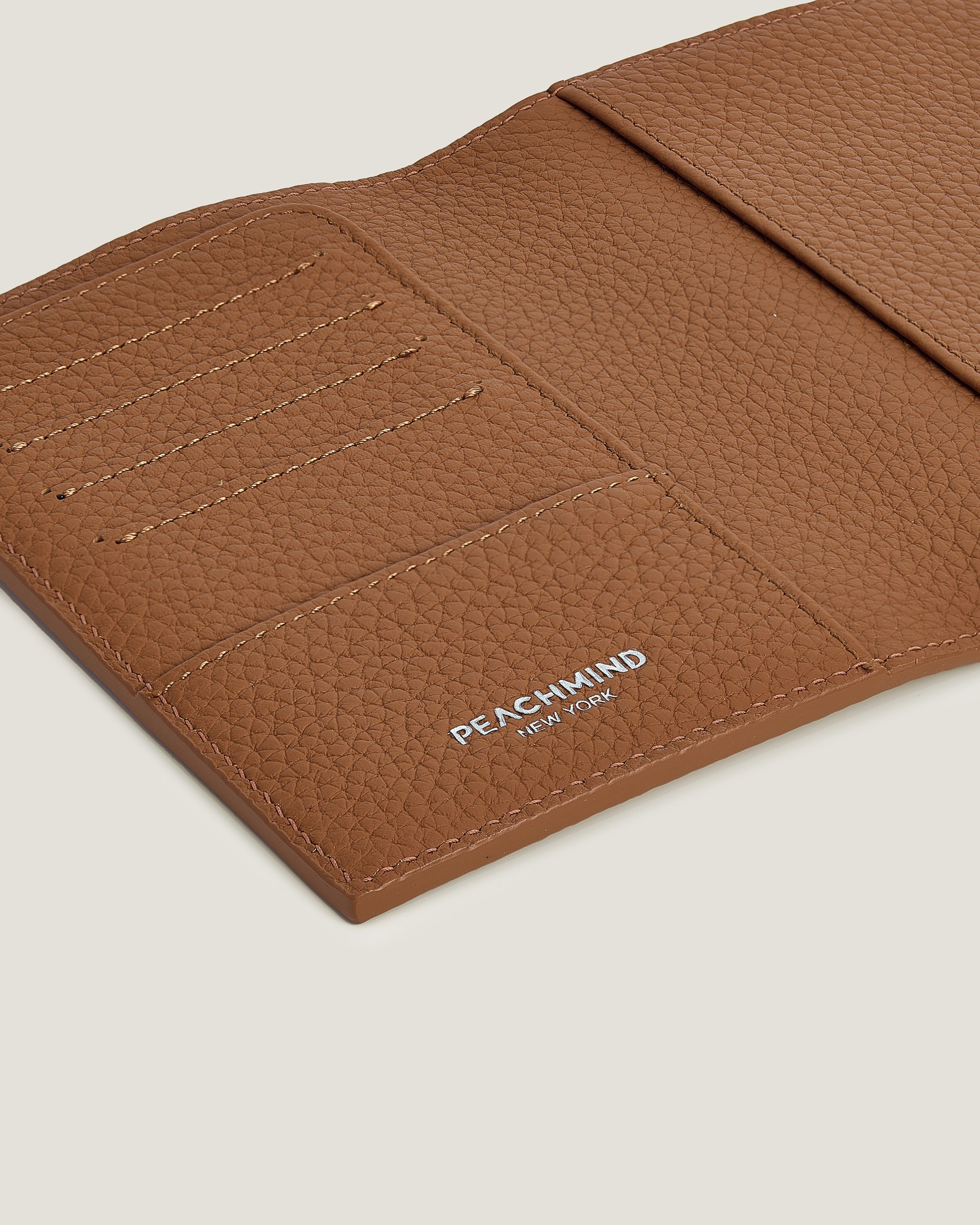Brown leather wallet with 'Peachmind' branding on a light beige background