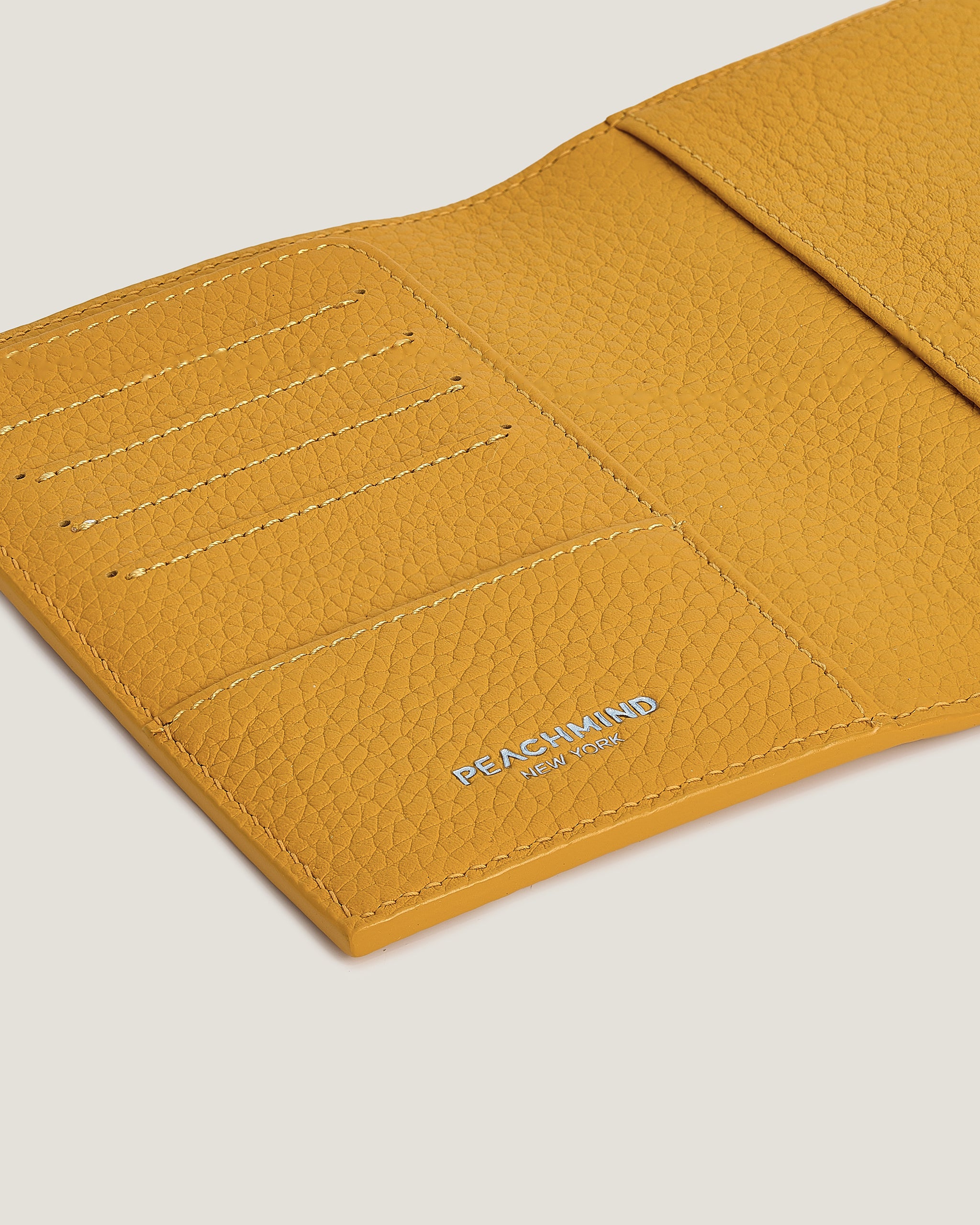 Close-up of a yellow leather wallet with 'Peachmind' branding on a light gray background